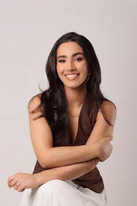 Ana Claudia Braga, fisioterapeuta pélvica, sentada e sorrindo, em fundo de estúdio.