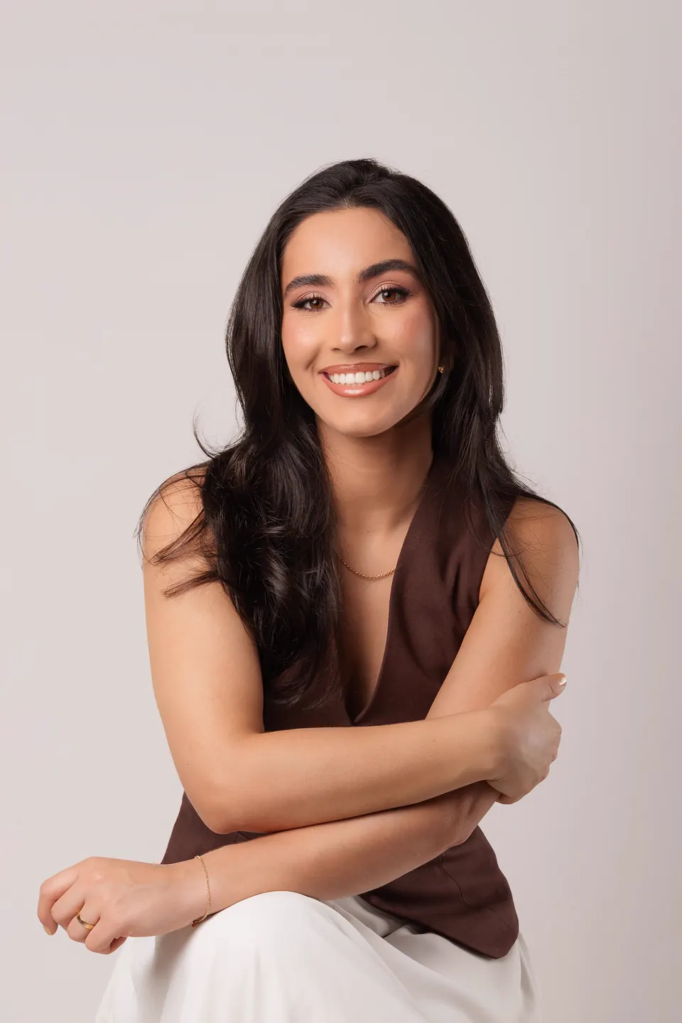 Ana Claudia Braga, fisioterapeuta pélvica, sentada e sorrindo, em fundo de estúdio.